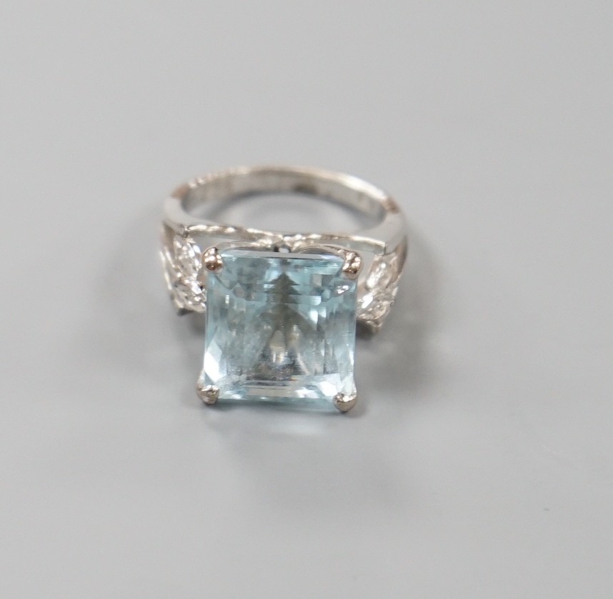 A white metal and single stone square cut aquamarine set dress ring, with diamond set shoulders, size K, gross weight 7 grams.